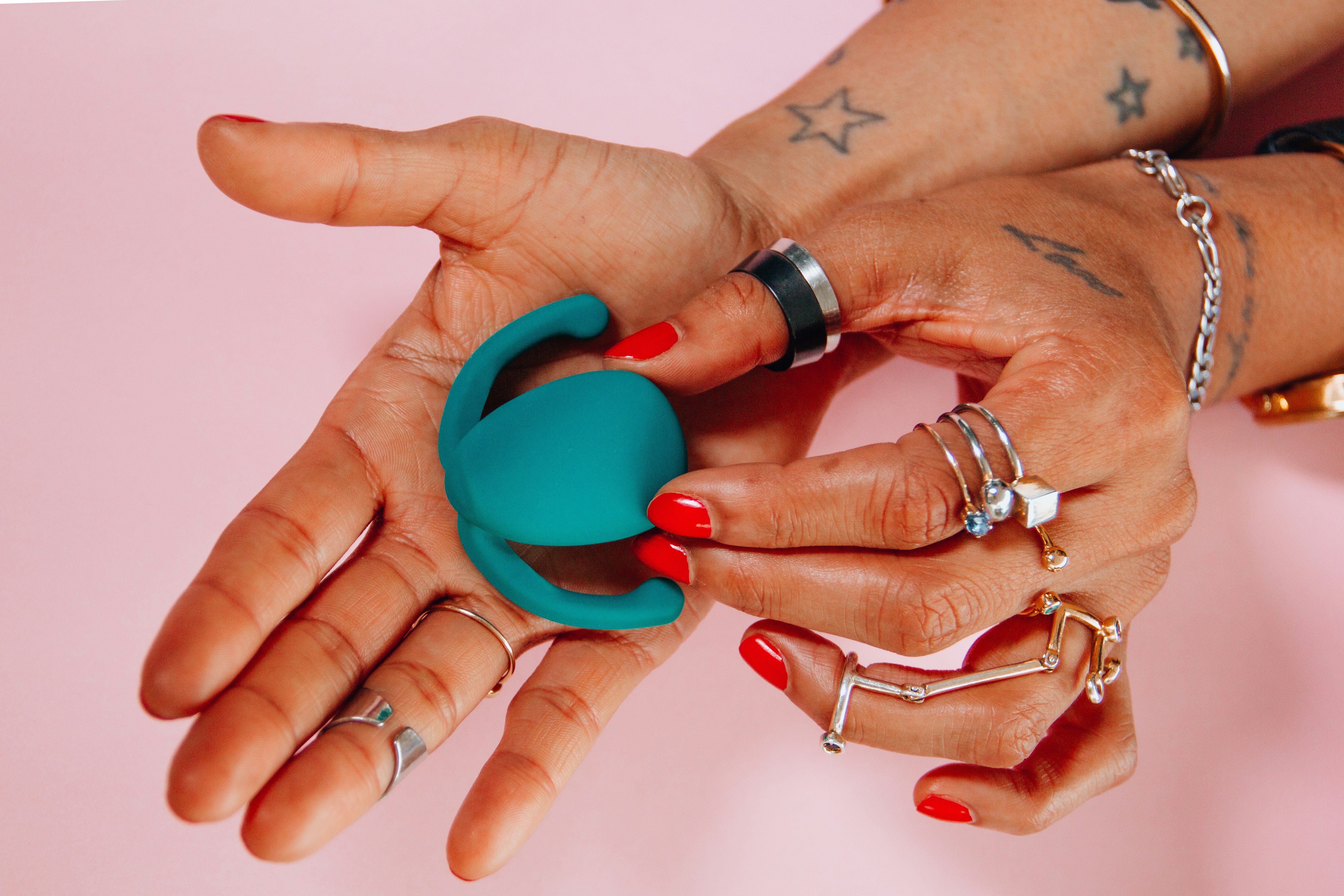 Mains tenant un petit stimulateur en silicone turquoise sur fond rose, illustrant la masturbation et le plaisir en solo