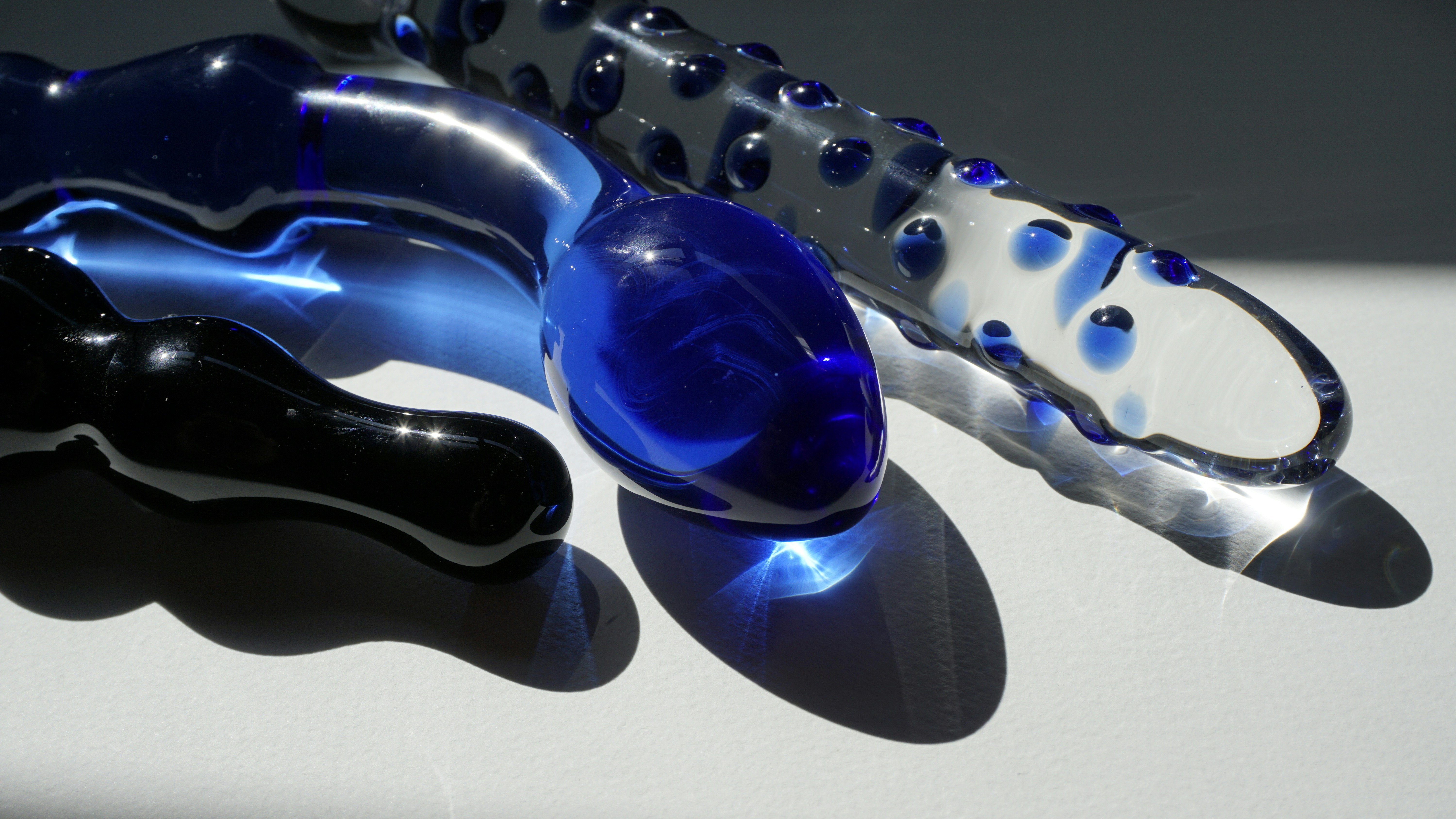 Trois jouets en verre bleu aux textures variées, posés sous une lumière qui joue avec la matière